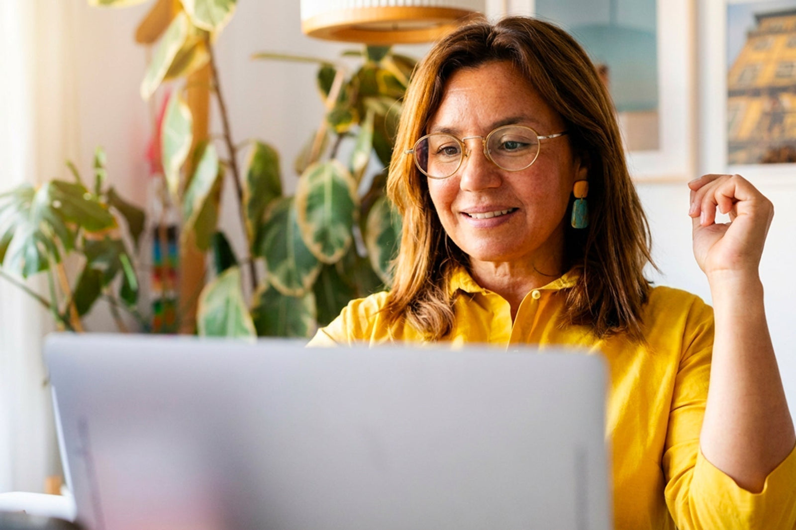 Woman over 40 in a yellow shirt smiling while reading about creatine on her laptop